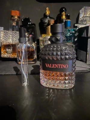 Valentino coral fantasy 10 ml sample - Säljer en lyxig parfym från Valentino i en snygg glasflaska med nitar och svart kork. Flaskan har en cool design med genomskinligt glas nertill och svart upptill, samt en tydlig Valentino-logga på framsidan. Perfekt för dig som gillar exklusiva dofter och stilren design. 10 ml bara