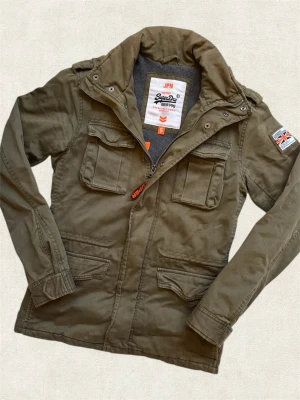 *UNIK* SUPERDRY FIEDLJACKET - En sällsynt fieldjacket av märket ”Superdry” med extremt bra passform! Fodrad vilket gör den perfekt året runt. Hör av dig vid frågor.