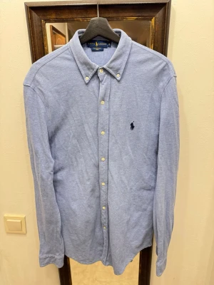 Ralph Lauren Skjorta - Klassisk ljusblå skjorta från Ralph Lauren med button-down krage och broderad logga på bröstet. Skjortan har långa ärmar och knäppning framtill. Tillverkad i ett lätt och bekvämt bomullsmaterial.