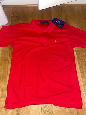 Ny Röd pikétröja från Polo Ralph Lauren - Hej! Säljer nu denna Klassiska röda pikétröja från Polo Ralph Lauren med gul broderad logga på bröstet. Jag hade fått denna i present men kommer tyvärr inte åt andvändning. 