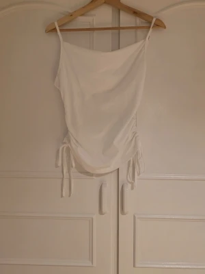 Vit linnetopp med snörning i sidan - Säljer en vit linnetopp med tunna axelband och snygg snörning i sidorna. Toppen har en lös passform upptill.