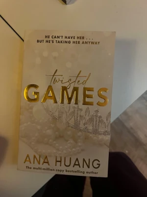 Twisted Games av Ana Huang - Twisted Games är en romantisk skönlitterär bok av Ana Huang. Omslaget är beige med guldfolierad text och dekorerat med pärlor och en krona. Perfekt för dig som gillar spännande och känslosamma berättelser.