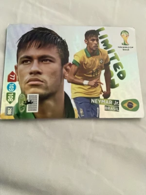 Panini Neymar Jr. Limited Edition kort - Samlarobjekt: Limited Edition fotbollskort från Panini Adrenalyn, FIFA World Cup Brasil 2014. Kortet visar Neymar Jr. i Brasiliens landslagströja, med färgerna gult, grönt och blått. Perfekt för dig som gillar fotboll och samlarkort.