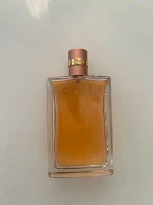 Chanel Allure Eau de Parfum - Chanel Allure Eau de Parfum i en elegant, rektangulär glasflaska med guld- och roséfärgad kork. Doften har en varm bärnstensfärgad vätska och flaskan har diskret Chanel-logga och Allure-tryck på framsidan. Perfekt för dig som gillar lyxiga och klassiska parfymer.