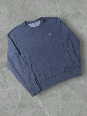 Blå sweatshirt från Polo Ralph Lauren - Mörkblå sweatshirt med rund hals från Polo Ralph Lauren. Tröjan har lång ärm och klassisk broderad logga på bröstet. Tillverkad i mjukt bomullsmaterial och har ribbade muddar vid ärmslut och nederkant. Perfekt för en avslappnad och stilren look.