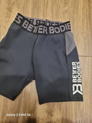 Svarta Better Bodies träningsshorts - Snygga svarta träningsshorts med bred resår i midjan och vit logga på benet. Shortsen har en tight passform och är gjorda i ett stretchigt syntetmaterial som passar perfekt för gym eller annan träning.