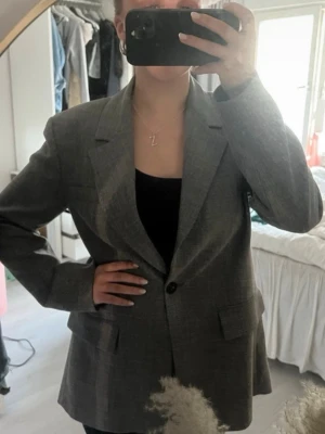 Grå oversized kavaj/blazer - Snygg grå oversized kavaj med klassiska slag och enkelknäppning. Kavajen har två fickor framtill och en rak passform som ger en cool och avslappnad stil. Perfekt att slänga över en t-shirt eller topp för en trendig look.