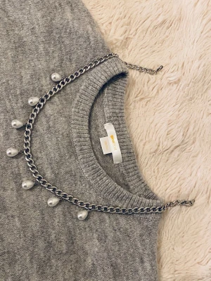 Silverfärgat halsband med pärlor - Stilrent halsband i silverfärgad metall med kedja och sju droppformade vita pärlor som hänger längs kedjan. Perfekt accessoar för att lyfta din outfit med en modern och trendig touch.