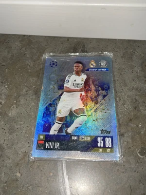 Match Attax fotbollskort Vinícius Jr. - Säljer ett glittrigt Match Attax samlarkort från Topps med Vinícius Jr. i Real Madrid C.F. 2023/24. Kortet har holografisk yta, visar spelarens stats och klubbmärke. Perfekt för dig som samlar på fotbollskort eller älskar Champions League.