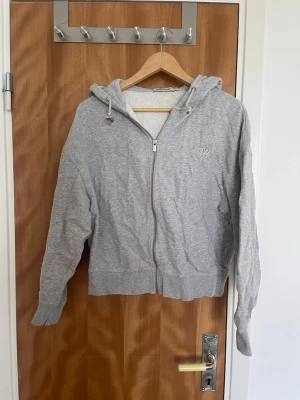 Grå zip-hoodie från CW - Snygg grå hoodie med dragkedja från OW. Hoodien har huva med dragsko, ribbade muddar och en liten broderad CW-logga på bröstet. Perfekt för en avslappnad och chill stil. Tillverkad i mjukt bomullsmaterial.