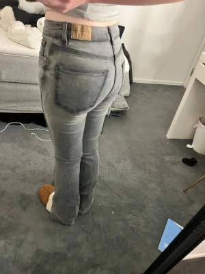Gråa bootcut jeans med hög midja - Säljer ett par gråa bootcut jeans med hög midja och klassiska fem fickor. Jeansen har en snygg tvättad look och är tillverkade i denim. Passar perfekt till en avslappnad stil och är riktigt bekväma.