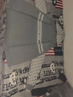 Grå hoodie  - Snygg grå hoodielogga på bröstet och unikt mönster i vitt och grått på ärmar och huva. Hoodien har klassisk passform, ribbade muddar och en stor huva. Perfekt för dig som vill sticka ut med exklusiv streetstyle.
