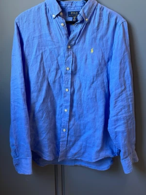 Blå linneskjorta Polo Ralph Lauren - Tja! Säljer en klassisk blå skjorta från Polo Ralph Lauren. Jag har endast testat den på och säljer pågrund av att den var för liten.Skjortan är i linne med button-down krage och gul broderad logga på bröstet. Skjortan har vita knappar framtill. Perfekt för en avslappnad men ändå stilren look.