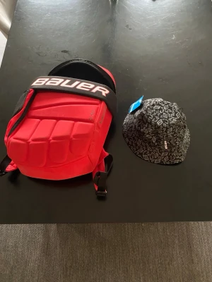 Svart bucket hat från Bauer och rygg säck  priset är för båda kan säljas enskilt  - Säljer en svart bucket hat från Bauer med coolt mönster i vitt och grått. Hatten har en klassisk form med bred brätte och är tillverkad i ett lätt tygmaterial. Perfekt för dig som vill ha en sportig och trendig look.