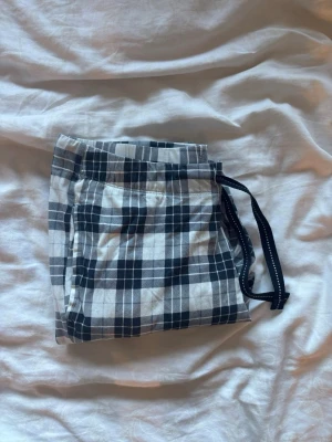 Rutiga pyjamasbyxor med dragsko - Mysiga pyjamasbyxor i svartvitt rutigt mönster med elastisk midja. Lite defekter som fläck och sedan ett ihopsytt hål som varken känns eller syns på avstånd