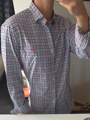 Rutig skjorta från Polo Ralph Lauren - Snygg rutig skjorta från Polo Ralph Lauren i bomull. Skjortan har klassisk krage, knappar framtill och lång ärm. Färgerna är blå, röd, grön och vit i ett fräscht rutmönster. Perfekt för en stilren och avslappnad look. Den är lite missfärgad i kragen, därav priset. Annars bra skick 