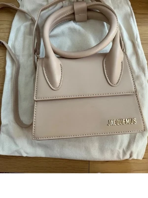 Beige Jacquemus Le Chiquito handväska - Superfin beige Jacquemus Le Chiquito handväska i slät läder med guldfärgad logga framtill. Väskan har ett topphandtag och en lång axelrem så du kan bära den på flera sätt. Stilren och trendig design som verkligen sticker ut.