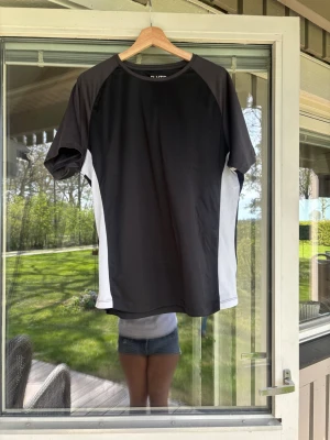 Svart och vit sporttröja från ELVTD - Sportig t-shirt från ELVTD i svart med vita paneler på sidorna och ryggen. Tillverkad i ett lätt och snabbtorkande material, perfekt för träning eller löpning. Klassisk rund hals och korta ärmar för maximal rörelsefrihet.