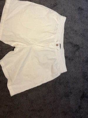 Vita bomullsshorts med snörning - Snygga vita shorts i bomull med elastisk midja och snörning framtill. Klassisk och enkel design med fickor på sidorna, perfekta för sommardagar. Passar dig som gillar en avslappnad och clean stil.