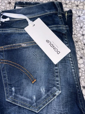 Mörkblå jeans från Dondup - Snygga mörkblå jeans från Dondup med slitna detaljer och kontrastsömmar. Klassisk femficksmodell i stretchigt denimtyg. Perfekta för en avslappnad och trendig look.