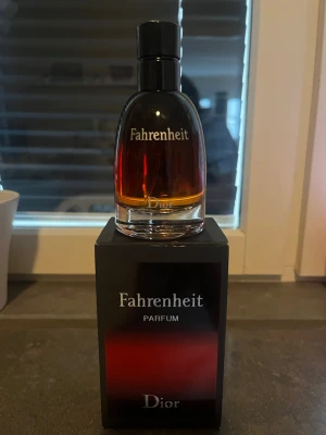 Dior Fahrenheit Parfum 75ml - Dior Fahrenheit Parfum i en elegant glasflaska med svart kork och rödtonad vätska. Flaskan rymmer 75 ml och kommer i en snygg svart kartong med röda detaljer. En ikonisk doft som utstrålar stil och karaktär.