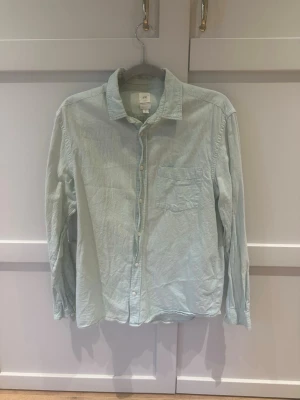 Ljusgrön skjorta - En stilren ljusgrön skjorta från H&M i bomull och linne. Skjortan har klassisk krage, knäppning framtill och en bröstficka.