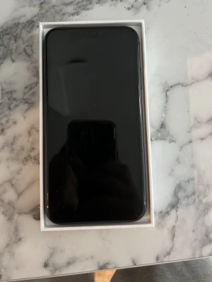 Svart iPhone 11  - Säljer en svart iPhone 11 från Apple. Telefonen har en stilren design med rundade kanter och glasbaksida. Hittade inte original förpackningen men skickar i min iPhone 13 låda. Slänger också med ett silikonskal i bra skick