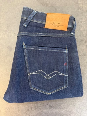 Mörkblå jeans från Replay W32 - Snygga mörkblå jeans från Replay med klassisk femficksdesign och kontrastsömmar. Jeansen har en rak passform och detaljerad bakficka med broderi samt läderpatch med logga i midjan. Tillverkade i denim med en stilren look.Mått  Midja (platt): 42 cm  Innerbenslängd: 70 cm  Lårvidd (10 cm från gren): 24 cm  Benöppning: 17 cm  Grenhöjd: 27 cm  Total längd: 94 cm