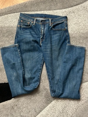 Blå Levi's 501 jeans - Säljer ett par klassiska blå Levi's 501 jeans med raka ben och femficksdesign. Jeansen har en snygg vintage-look, tydliga sömmar och den ikoniska läderpatchen bak i midjan. Materialet är slitstark denim i bomull och passformen är tidlös och bekväm.