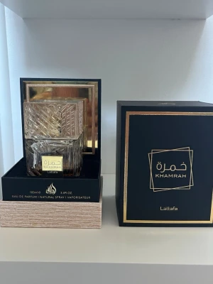 Lattafa Khamrah Eau de Parfum 100ml - Lattafa Khamrah Eau de Parfum i en lyxig, fyrkantig glasflaska med detaljerat mönster och guldfärgad etikett. Kommer i en elegant svart och guld ask med exklusiv känsla. Perfekt för dig som gillar unika och trendiga dofter. 50ml kvar ca