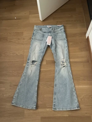 Ljusblå utsvängda jeans Gina Tricot - Trendiga ljusblå bootcut jeans  från Gina Tricot med utsvängda ben och slitna detaljer på båda knäna. Jeansen har låg midja . Perfekta för dig som gillar en avslappnad och cool stil. Den är i S men passar även xs jag är 162 cm och passar mig perfekt 
