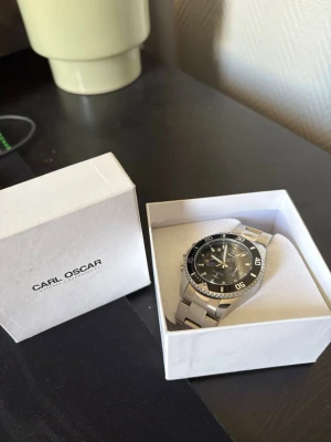 Silverfärgad klocka från TRSOYE - Stilren klocka från TRSOYE med svart urtavla och silverfärgat armband i metall. Klockan har tydliga siffror och markeringar på ringen, samt flera små urtavlor för extra funktioner. Perfekt accessoar för dig som gillar en sportig och klassisk look.