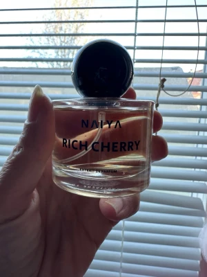 Naiya Rich Cherry Extrait de Parfum - Naiya Rich Cherry Extrait de Parfum i en rund, genomskinlig glasflaska med svart klotformad kork. Doften har en bärnstensfärgad vätska och flaskan har stilren svart text. Perfekt för dig som gillar fruktiga och lyxiga dofter.endast testad 
