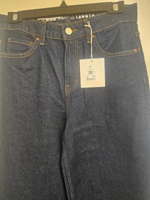 Mörkblå wide leg jeans från H&M - Snygga mörkblå jeans från H&M med wide leg-passform och hög midja. Klassisk femficksmodell med kontrastsömmar och knappgylf. Perfekta för dig som gillar en avslappnad och trendig stil.