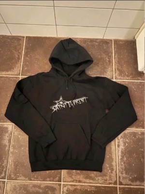 Svart Saint Laurent hoodie🤩🙌 - Svart hoodie från Saint Laurent med stort vitt grafiskt tryck på bröstet. Klassisk huva med dragsko och känguruficka framtill. Perfekt för en streetwear-look och tillverkad i mjukt material för extra komfort.🤩🙌
