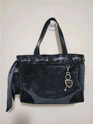Juicy Couture daydreamer scottie tote  - Juicy Couture handväska i svart sammet med detaljer i svart läder och silverfärgade metalldelar. Väskan har broderad logga framtill, dekorativt band och en hjärtformad nyckelring med Juicy Couture-tryck. Perfekt för dig som gillar en trendig och lyxig look.