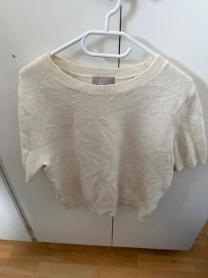 Vit stickad topp från H&M - Säljer en enkel och stilren vit stickad topp från H&M. Toppen har korta ärmar, rund halsringning och är gjord i ett mjukt material som känns skönt mot huden. Perfekt att matcha med jeans eller kjol för en clean look.