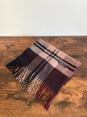 Burberry Halsduk - Vintage Burberrys halsduk i 100% lambswool. Made in England. Klassisk check i mörkare/bruna toner med diskret och tidlös look. Väldigt bra skick med endast mindre tecken på användning. Perfekt för en clean casual/old money stil.