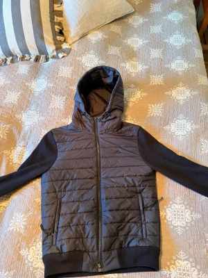 Svart j lindberg quiltad hoodie cardigan - Svart cardiganjacka med quiltad framsida och huva. Jackan har dragkedja, två fickor med dragkedja och mjuka ärmar i sweatshirtmaterial. Perfekt för lager-på-lager och streetstyle.  4000kr nu
