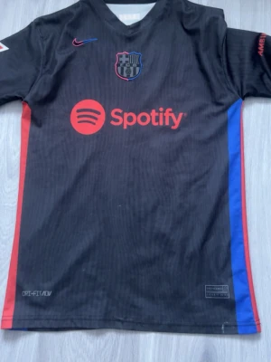 FC Barcelona svart matchtröja Nike - Svart FC Barcelona matchtröja med röda och blå detaljer, Nike-logga och Spotify som sponsor framtill. Namn och nummer Lamine Yamal 19 på ryggen. Tillverkad i lätt och ventilerande Dri-FIT-material, perfekt för fotbollsträning eller match. Använd ett par gången men i bra skick 
