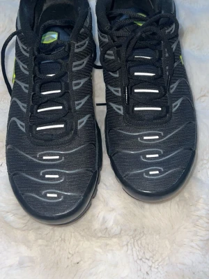 Nike Air Max Plus Tn Svart/Grå - Nike Air Max Plus Tn sneakers i svart mesh med grå och vita detaljer samt gula Tn-loggor på hälen. Köptes förra året men har inte kommit till mycket användning eftersom att jag hade andra skor. Den är i nästan nyskick med absolut inga defekter eller skador!