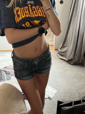 Mörkblå jeansshorts med låg midja - Snygga mörkblå jeansshorts med låg midja och klassiska fickor fram och bak. Shortsen har slitna detaljer och stängs med knapp och dragkedja. Perfekta för varma dagar och en avslappnad stil.