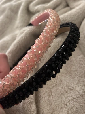 Två diadem med pärlor, rosa & svart - Säljer två snygga diadem, ett i ljusrosa med glittrande pärlor och ett i svart med svarta pärlor. Båda har en bred, vadderad form och är täckta av små, facetterade plastpärlor som ger en lyxig känsla. Perfekta för att lyfta vilken outfit som helst.