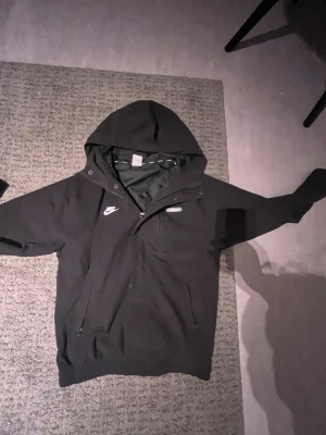 Svart Nike Air Max vindjacka med huva - Svart vindjacka från Nike Air Max med huva och dragkedja framtill. Nypris 1300kr. Inga tecken på användning. Egentlig storlek S men passar jätte bra på mig som har M.