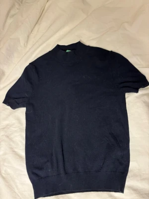 Mörkblå stickad tröja med kort ärm - En enkel och stilren mörkblå stickad topp med korta ärmar och hög hals. Perfekt till jeans eller kjol för en clean look. Mjuk och bekväm med ribbade kanter vid ärmslut och nederkant. Kashmir blandning köpte för 800