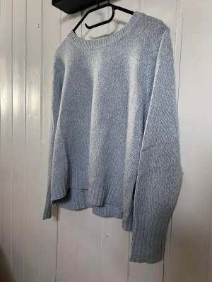 Ljusblå stickad tröja med rund hals - Mysig ljusblå stickad tröja med rund halsringning och långa ärmar. Tröjan har ribbade muddar vid ärmslut och nederkant samt en avslappnad passform. Perfekt för kyliga dagar och enkel att matcha med olika outfits.