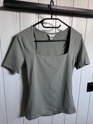 Grön topp med fyrkantig urringning H&M - Snygg grön topp från H&M med korta ärmar och fyrkantig urringning. Tillverkad i mjuk bomull som känns skön mot huden. Enkel och stilren design som passar till det mesta. Perfekt att matcha med jeans eller kjol.