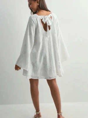 Vit kort klänning med rosett - Superfin vit kortklänning med vida ärmar och snygg rosettdetalj i ryggen. Klänningen har ett subtilt blommönster i tyget och är perfekt för sommaren och student (går att diskutera priset)