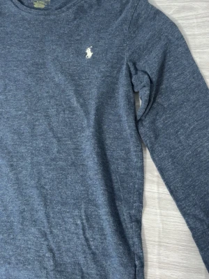 Mörkgrå långärmad tröja Polo Ralph Lauren - Mörkgrå långärmad tröja från Polo Ralph Lauren med klassisk rund halsringning och den ikoniska vita logobrodyrn på bröstet. Tillverkad i mjukt material som känns skönt mot huden. Perfekt för en avslappnad och stilren look.