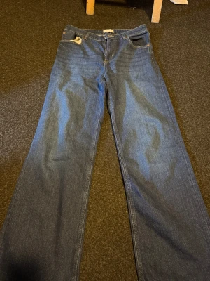 Blå raka jeans från H&M - Säljer ett par klassiska blå jeans från H&M i rak modell. Jeansen har normal midja, fem fickor och stängs med dragkedja och knapp. Tillverkade i denim med snygg tvätt och kontrastsömmar. Perfekta till en avslappnad look.